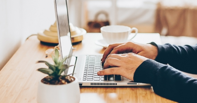 close up of man's hands typing on a desk at home